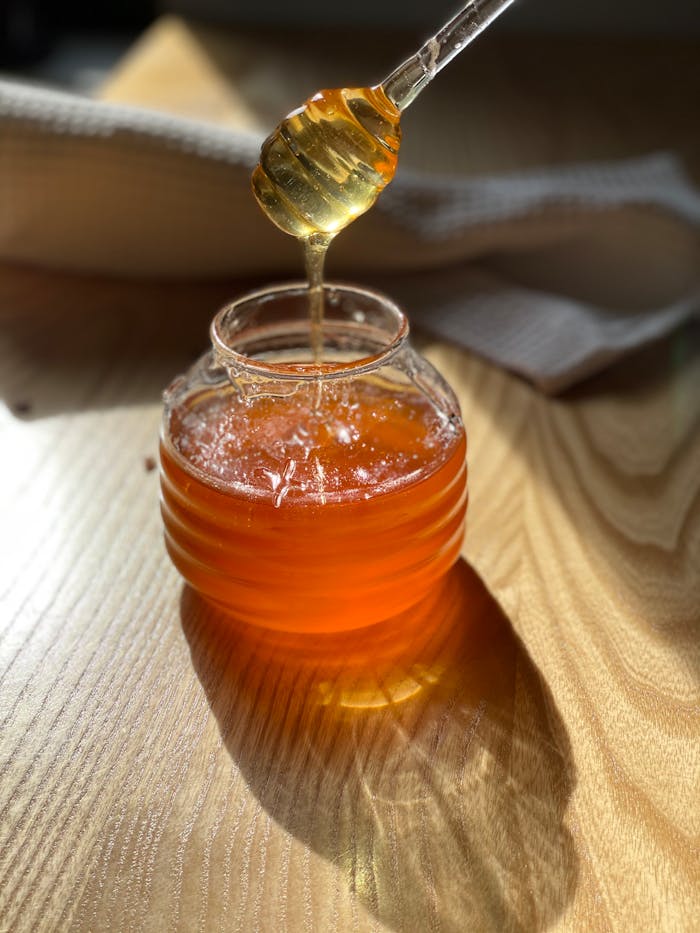 Close-up of honey drizzling into a glass jar on a wooden table, ideal for food and lifestyle themes.