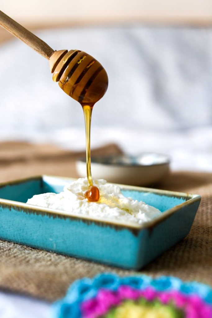 Close-up of honey being drizzled onto a dish of creamy cheese, highlighting its rich texture.