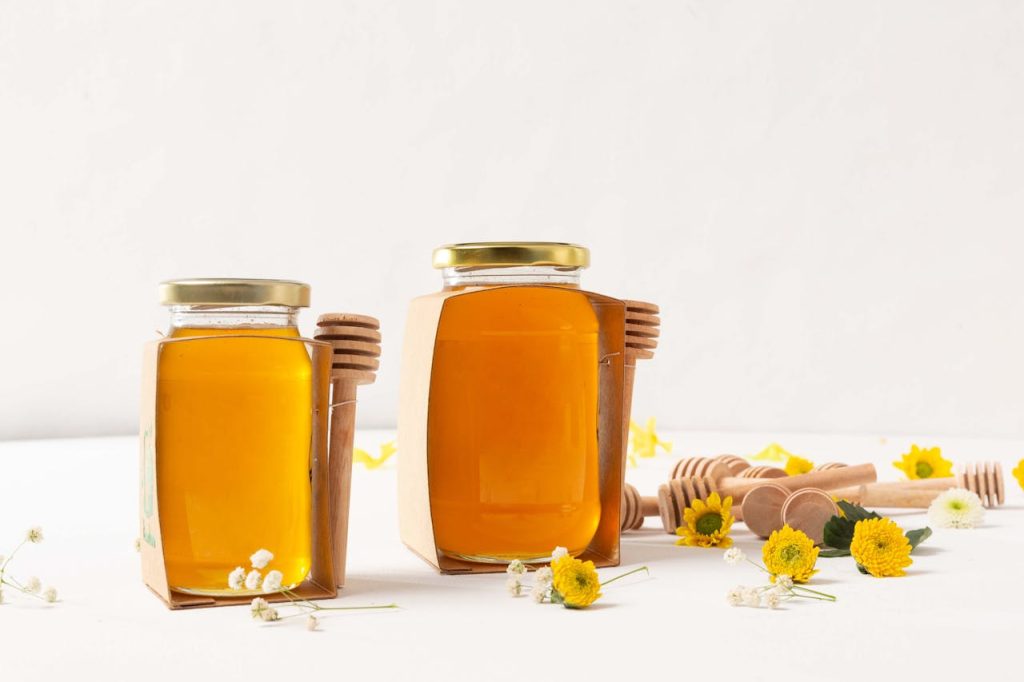 Aesthetic portrayal of honey jars with dippers and flowers on a white background.