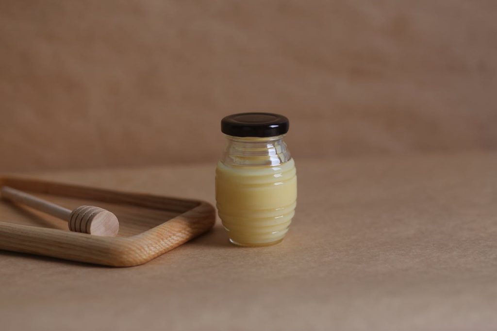 A glass jar of honey with a wooden dipper on a warm brown surface, offering an organic and homemade vibe.